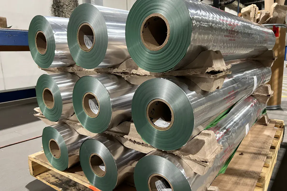 Stacked rolls of silver barrier foil used for corrosion protection in industrial packaging.