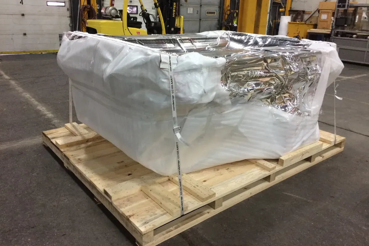 Industrial equipment wrapped in barrier foil and foam, secured to a wooden skid.