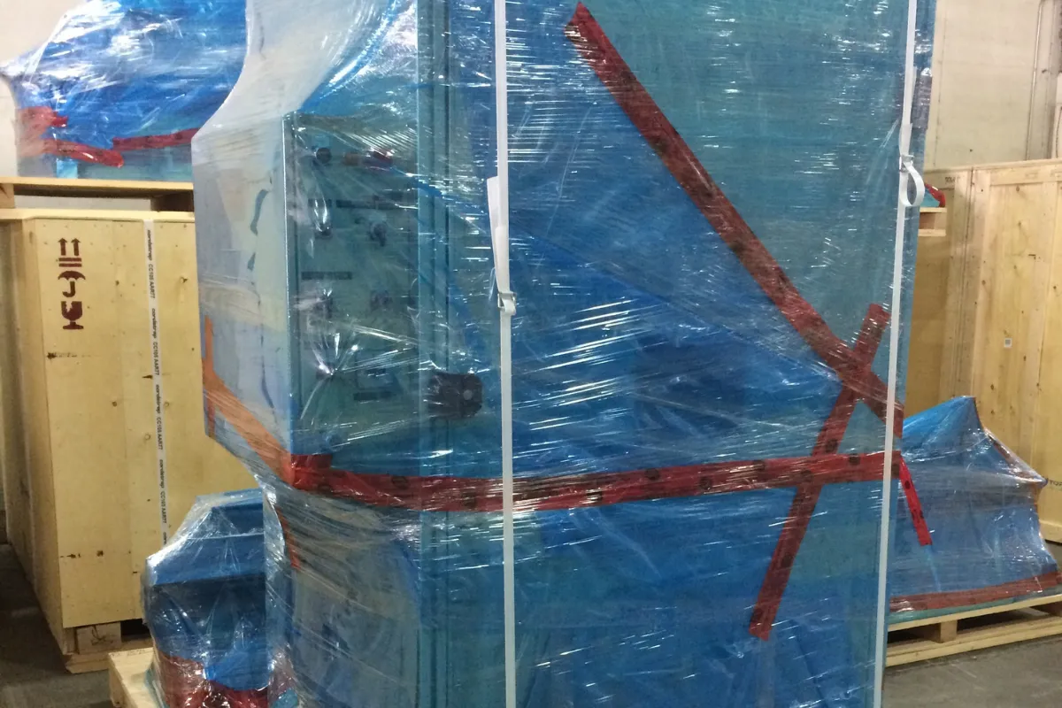 Machinery wrapped in blue corrosion protection film and secured with plastic strapping on a wooden base.